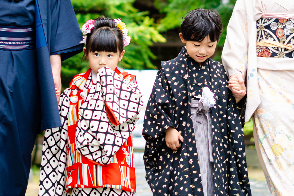 紺色のアンサンブルを着た男性と赤い被布を着た女の子と黒い羽織袴を着た男の子とクリーム色の訪問着を着た女性