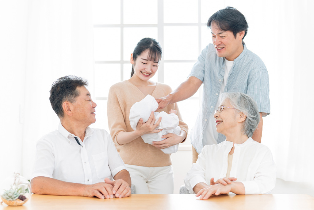 赤ちゃんを抱っこする女性と見守る男性と高齢男女