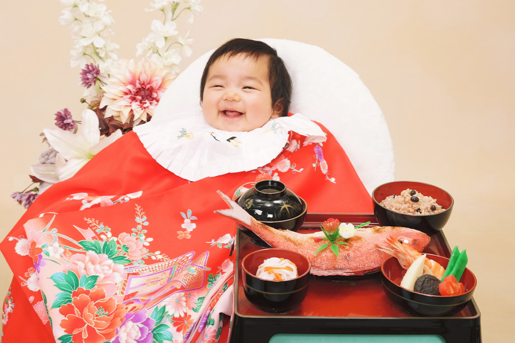 お食い初めの祝膳と赤い産着を着た赤ちゃん