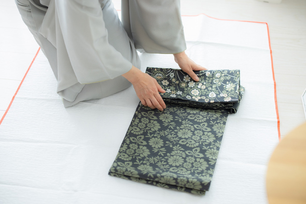 衣裳敷の上で帯をたたむ女性